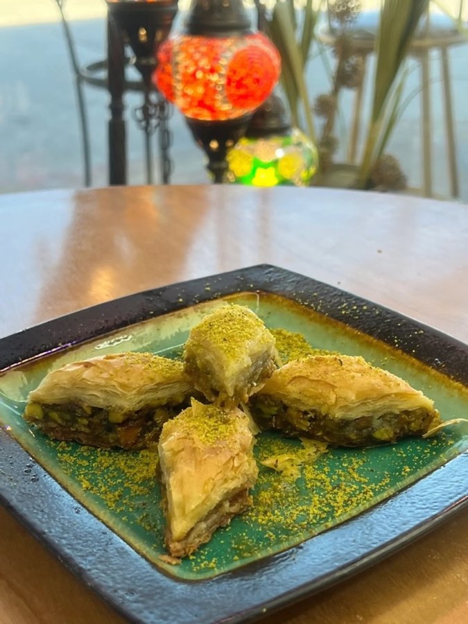 Pistachio baklava on a green ceramic plate beside Turkish mosaic lamps