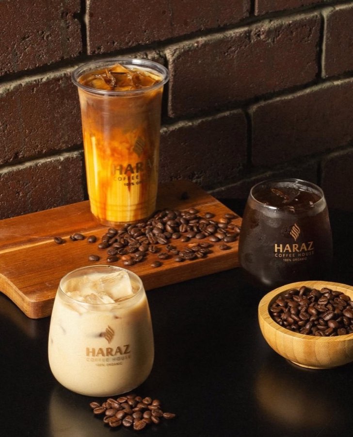 Three iced coffee drinks in Haraz-branded cups with coffee beans on a wooden board