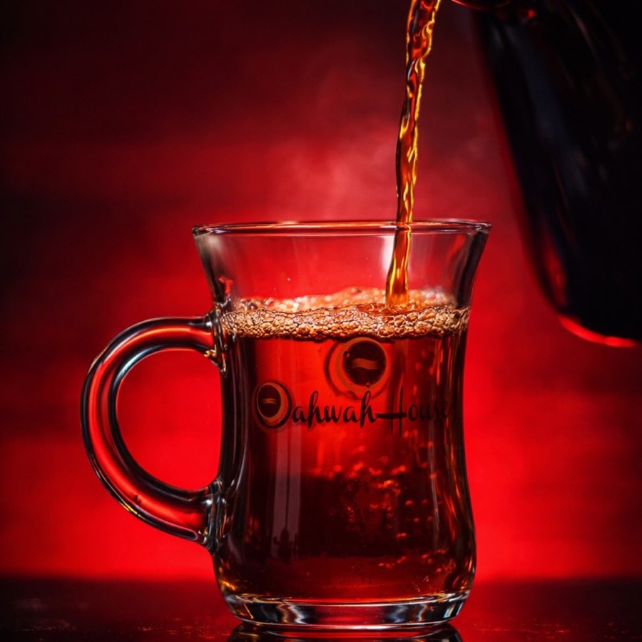 Hot amber-colored drink poured into a branded Qahwah House glass mug
