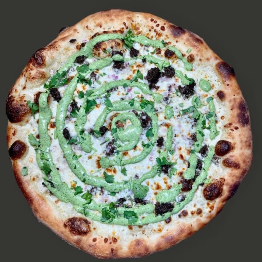 Pizza topped with crumbled meat, cilantro and a green sauce spiral