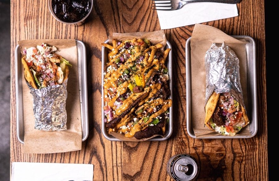 Spitz gyros and loaded fries on metal trays across a wooden table.