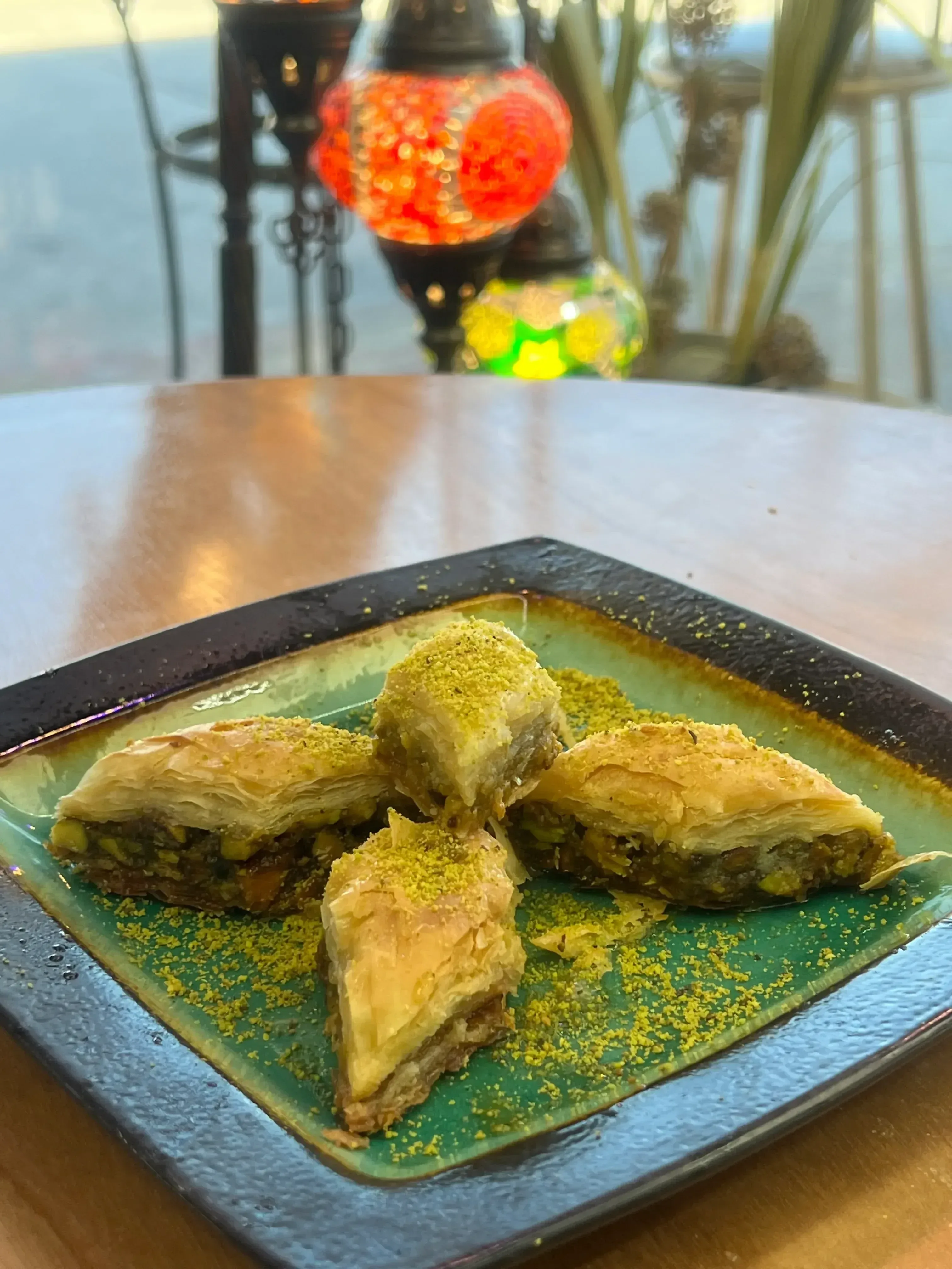 Pistachio baklava on a green ceramic plate beside Turkish mosaic lamps