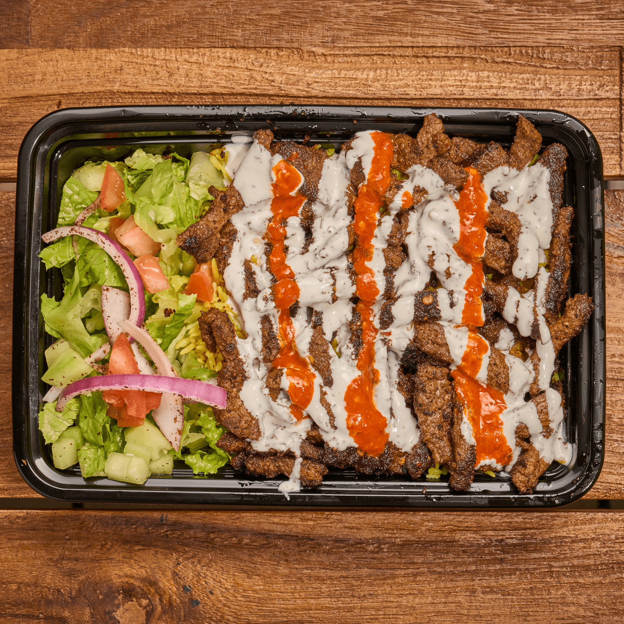 Seasoned beef over yellow rice with white and red sauces and a side salad