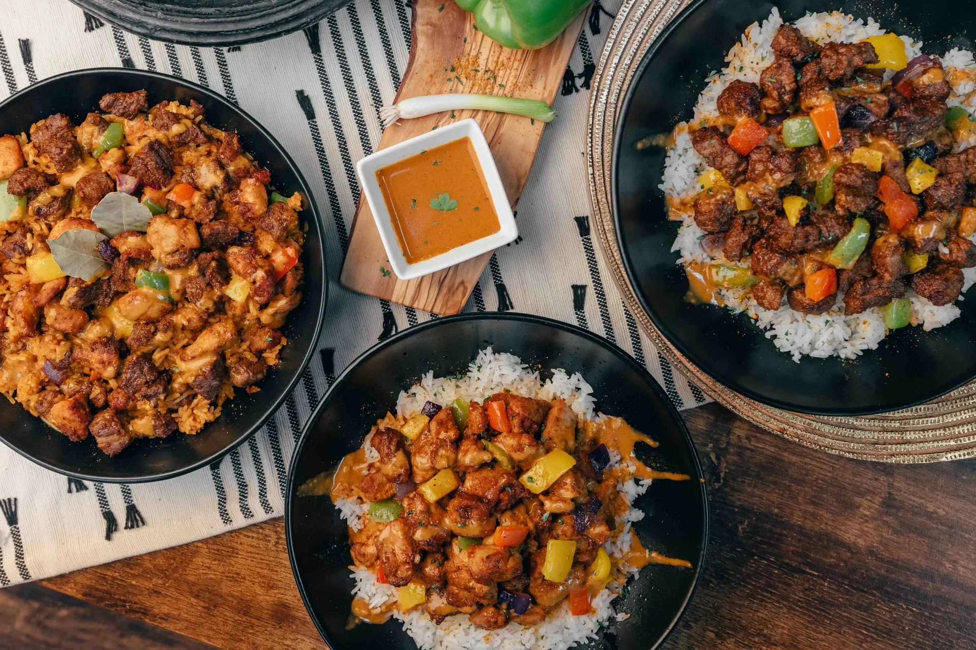 Three rice bowls topped with seasoned meat, peppers and orange sauce