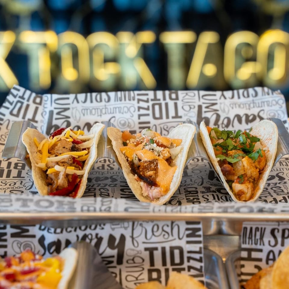 Three filled tacos on a tray with Tick Tock Taco signage behind them